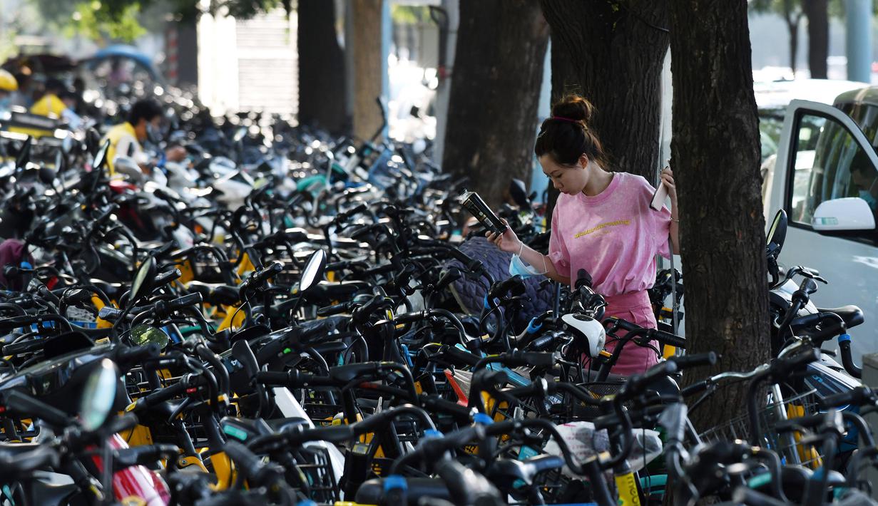 Seorang wanita berjalan melintasi sepeda-sepeda yang diparkir di atas trotoar di Beijing, China (21/7/2020). Seperti diketahui Beijing telah menerapkan bike sharing yang sudah tersedia di trotoar-trotoar Kota Beijing. (AFP Photo/Greg Baker)