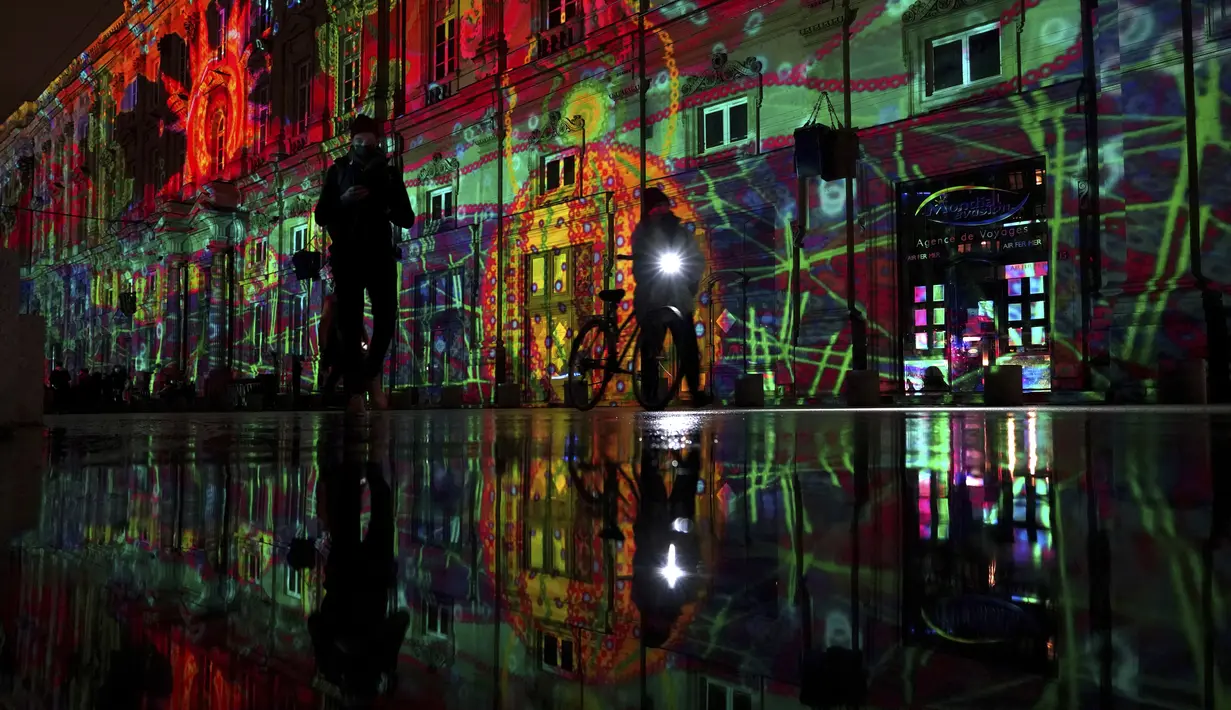Orang-orang melewati pertunjukan cahaya malam di Lyon, Prancis tengah, Rabu (8/12/2021). Jutaan orang diperkirakan akan menghadiri acara Festival of Lights selama empat hari di kota itu. (AP Photo/Laurent Cipriani)
