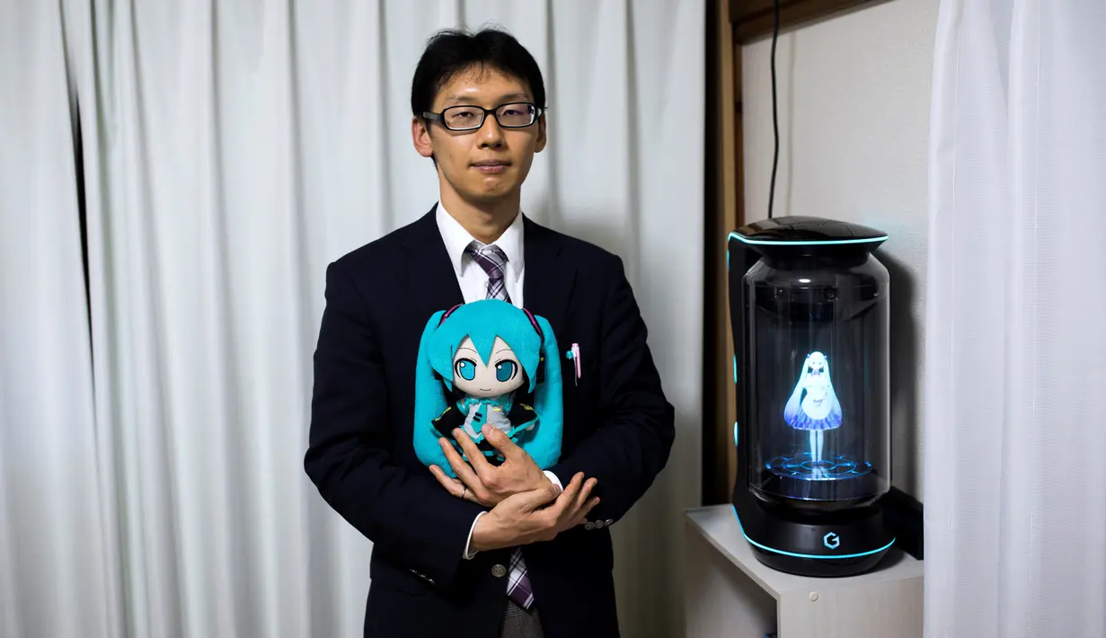 Akihiko Kondo asal Jepang berpose di sebelah hologram aktris virtual, Hatsune Miku sambil memegang versi bonekanya di Tokyo, 10 November 2018. Kondo memutuskan menikahi boneka karena mengalami kesulitan berinteraksi di tempat kerjanya. (Behrouz MEHRI/AFP)