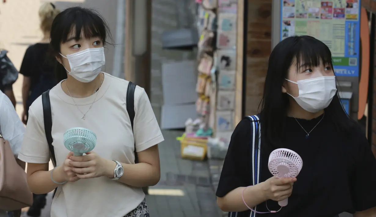 Dua wanita memakai masker wajah untuk membantu melindungi dari penyebaran coronavirus memegang kipas angin portabel untuk menghindari panas di Tokyo, Rabu, (5/8/2020). (AP Photo/Koji Sasahara)