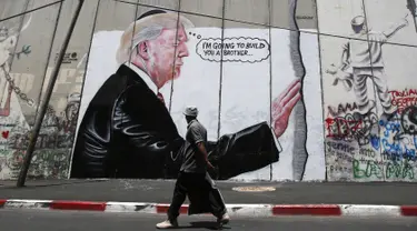 Seorang pria Palestina berjalan didepan grafiti yang menggambarkan Presiden AS Donald Trump di tembok pemisah Israel - Palestina di kota Bethlehem (4/8). Tembok di Tepi Barat ini membentang sepanjang 700 kilometer. (AFP Photo/Musa Al Shaer)