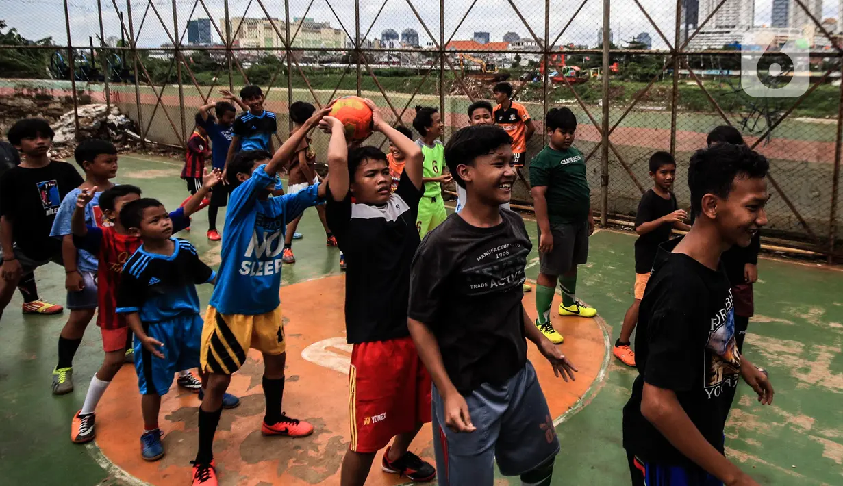 Anak-anak berlatih sepak bola di lapangan samping Banjir Kanal Barat (BKB), Jakarta, Kamis (7/1/2020). Revitalisasi jalur hijau di sepanjang aliran BKB menyulap kawasan kumuh menjadi tempat interaktif warga sekitar yang dilengkapi fasilitas bermain, seperti lapangan futsal. (Liputan6.com/Johan Tallo