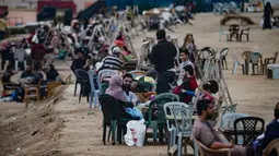 Warga Palestina berkumpul untuk berbagi makanan buka puasa selama bulan suci Ramadan, saat pandemi virus corona, di sepanjang pantai kota Gaza pada 13 Mei 2020. Mereka menunggu waktu berbuka puasa sambil menyaksikan matahari terbenam. (Photo by MAHMUD HAMS / AFP)