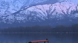 Orang-orang menikmati perjalanan dengan perahu dengan latar belakang pegunungan yang tertutup salju di danau Dal di Srinagar (11/1/2022). Daya tarik keindahan yang sempurna membuat danau Dal dijuluki sebagai Jewel in the Crown of Kashmir atau Srinagar Jewel. (AFP/Tauseef Mustafa)