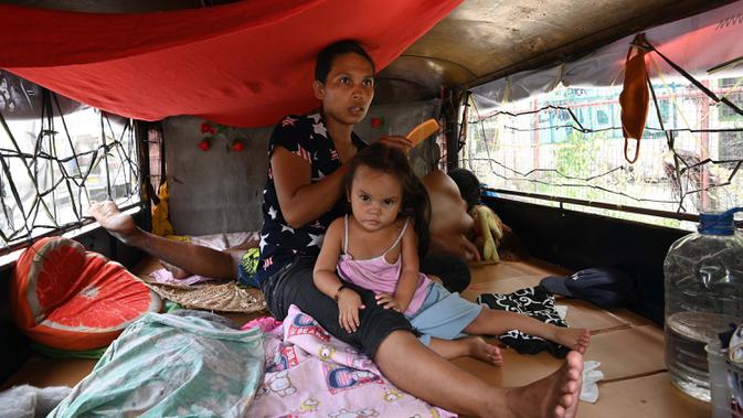 Istri pengemudi dan anaknya berada di dalam jeepney mereka yang berfungsi sebagai rumah sementara di Manila, 12 Agustus 2020. Angkutan ikonik di Filipina itu belum dapat mengangkut penumpang sejak Maret akibat lockdown Covid-19 yang membuat jutaan orang kehilangan pekerjaan. (Ted ALJIBE/AFP)