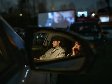 Sepasang suami istri duduk di mobil mereka ketika menonton pemutaran film di sebuah bioskop kendara atau drive-in cinema di Seoul, Korea Selatan, 21 Maret 2020. Jenis bioskop ini menjadi pilihan yang lebih bagi warga Seoul untuk menikmati film di tengah pandemi virus corona Covid-19. (Ed JONES/AFP)