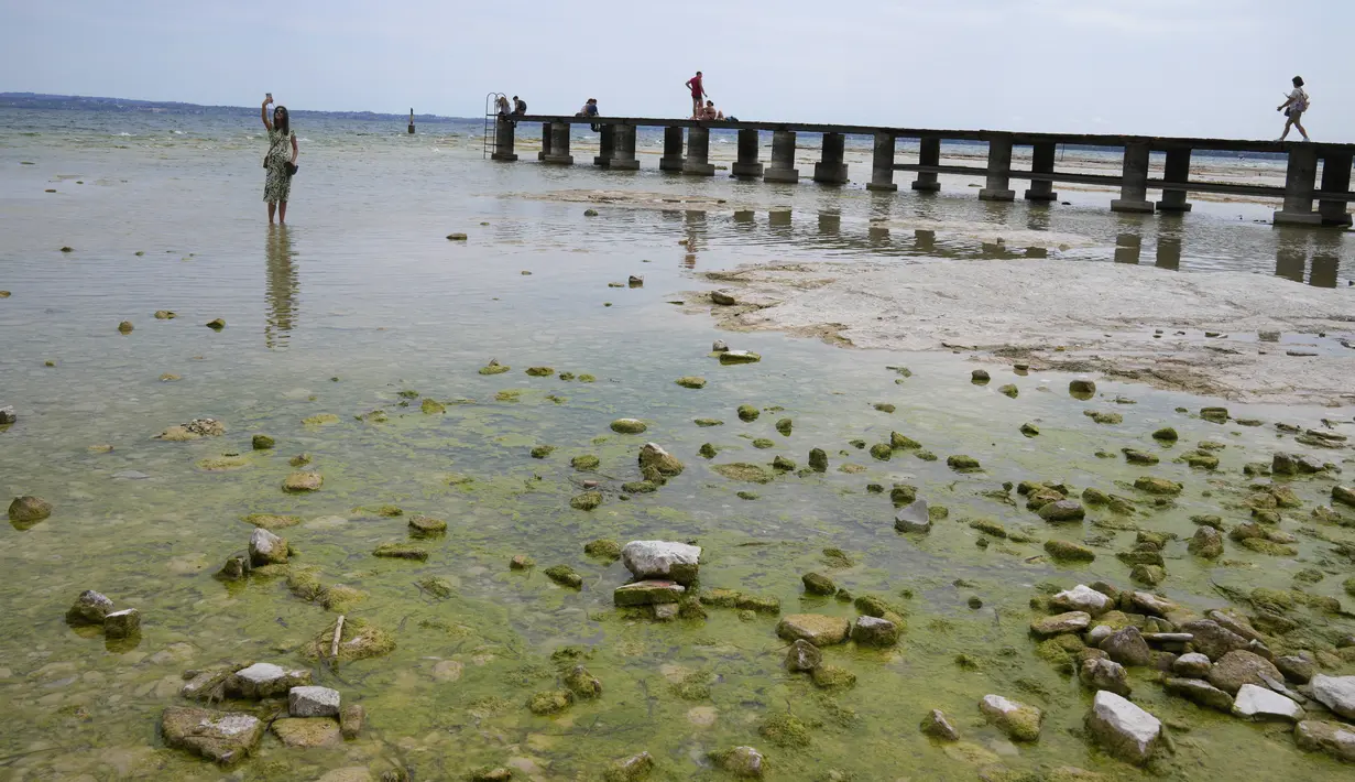 Seorang wanita berfoto selfie di semenanjung Sirmione, di danau Garda, Italia, Jumat (12/8/2022). Permukaan air Danau Garda telah turun secara kritis menyusul kekeringan parah yang mengakibatkan munculnya bebatuan di sekitar Semenanjung Sirmione. (AP Photo/Antonio Calanni)