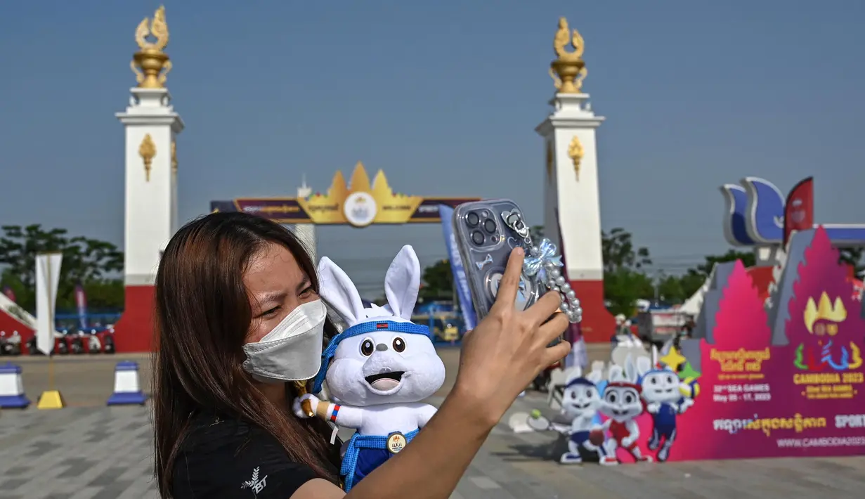 Bahkan, di tengah terik matahari seorang wanita menyempatkan berswafoto dengan maskot acara di luar Stadion Nasional Morodok Techo sesaat jelang upacara pembukaan Pesta Olahraga Asia Tenggara (SEA Games) ke-32 di Phnom Penh pada tanggal 5 Mei 2023. (NHAC NGUYEN/AFP)