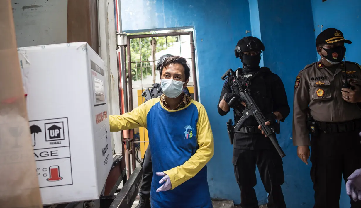 Polisi bersenjata bersiaga saat pekerja menurunkan vaksin COVID-19 produksi Sinovac dari truk setibanya di Surabaya pada Senin (4/1/2021).  Pemerintah mulai mendistribusikan 3 juta dosis vaksin Covid-19 asal perusahaan China, Sinovac, ke 34 provinsi Indonesia. (Photo by Juni Kriswanto / AFP)
