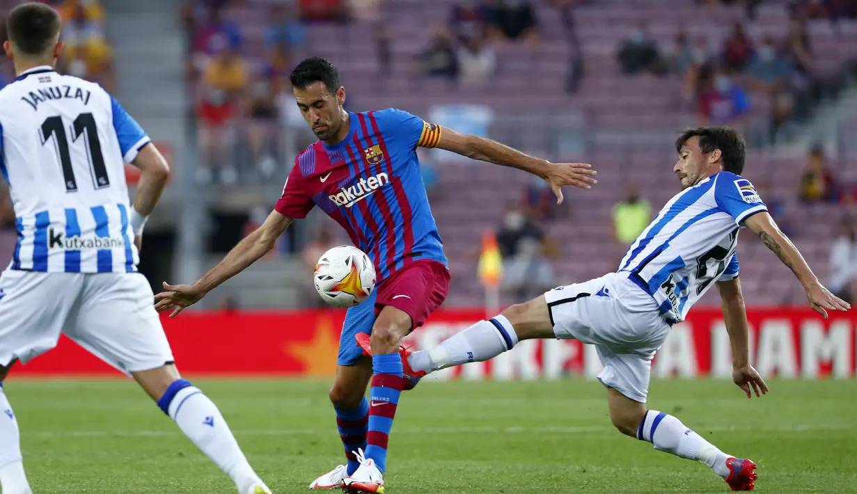 Gelandang Real Sociedad, David Silva berusaha merebut bola dari gelandang Barcelona, Sergio Busquets pada pertandingan La Liga Spanyol di stadion Camp Nou di Barcelona, Spanyol, Senin (16/8/2021). Barcelona menang atas Sociedad 4-2.  (AP Photo/Joan Monfort)