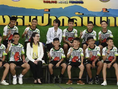 12 anak laki-laki dan pelatih sepak bola mereka, yang diselamatkan dari gua banjir di Thailand tampil ke muka publik untuk pertama kalinya di Chiang Rai, Rabu (18/7). Mereka memasuki ruang konferensi pers dengan memakai seragam. (LILLIAN SUWANRUMPHA /AFP)