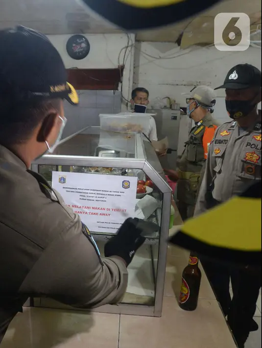 Petugas menempelkan stiker perautran "Take away"  di tempat makan di wilayah Kecamatan Pulogadung, Jakarta, Jumat (18/9/2020). Malam, Razia dilakukan memastikan ketidakadaannya konsumen makan ditempat tersebut. (merdeka.com/Imam Buhori)