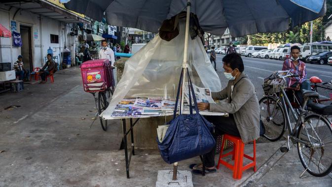 Seorang pria membaca koran di kiosnya sehari setelah militer Myanmar merebut kekuasaan, Yangon, Myanmar, Selasa (2/2/2021). Militer Myanmar menahan pemimpin yang terpilih secara demokratis Aung San Suu Kyi dan memberlakukan keadaan darurat satu tahun. (STR/AFP)