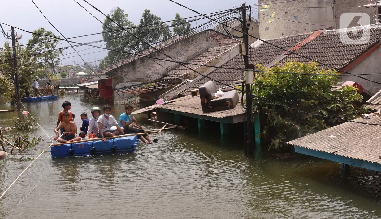 Warga melintas dengan perahu buatan saat banjir melanda perumahan Periuk Damai, Tangerang, Banten, Selasa (22/2/2021). Ratusan rumah masih terendam banjir sampai menyentuh ke atap rumahnya. (Liputan6.com/Angga Yuniar)