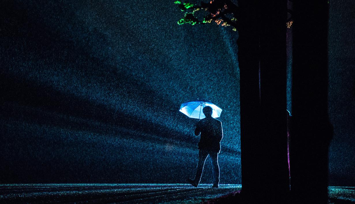 Pengunjung memakai payung saat berada di dekat seni instalasi cahaya "Painting the Night" karya seniman Austria Victoria Coeln saat hujan turun di taman Heruerhae Gaerten di Hanover, Jerman utara, (4/5). (AFP Photo/dpa/Silas Stein/Jerman Out)