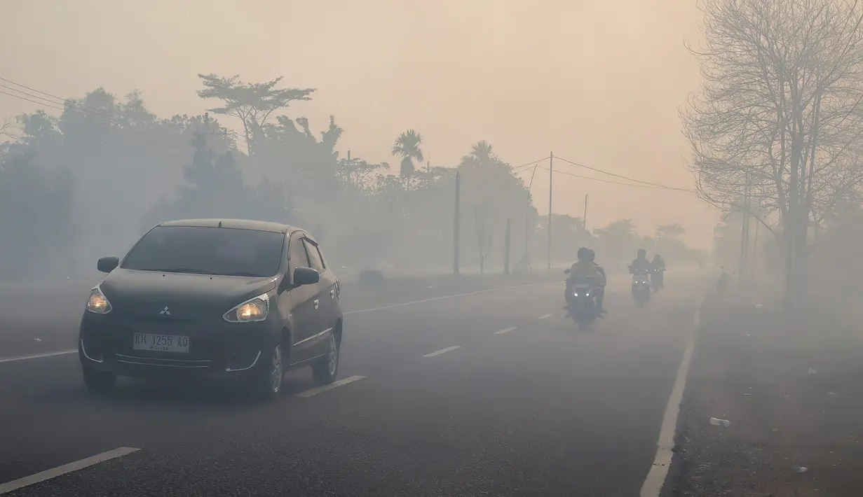 Para pengendara bermotor menyalakan lampu depan kendaraan saat melintasi jalan yang diselimuti kabut asap di Kota Palangka Raya, Kalimantan Tengah, Kamis,  20 Agustus 2026. (AFP/ Reina)