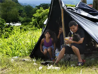 Seorang ayah memberi susu botol jus jeruk kepada putrinya yang masih bayi di tepi Sungai Huixtla, negara bagian Chiapas, Meksiko, Rabu (8/5/2022). Keluarga itu adalah rombongan dari kelompok migran, banyak dari Amerika Tengah dan Venezuela, yang meninggalkan Tapachula. (AP Photo/Marco Ugarte)