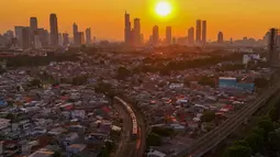 Rangkaian kereta melewati kawasan padat penduduk dengan latar belakang gedung bertingkat saat matahari terbenam di kawasan Manggarai, Jakarta, Kamis, 16/07/ 2026. (KLY/ Arie Basuki)