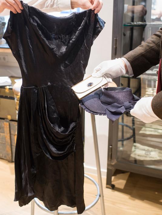 Pegawai memegang gaun, dompet, dan topi jerami milik pasangan Adolf Hitler, Eva Braun sebelum lelang memorabilia Nazi di Grasbrunn, Jerman, Rabu (20/11/2019). Busana-busana milik Eva Braun masing-masing terjual seharga beberapa ribu euro. (Matthias Balk/dpa via AP)