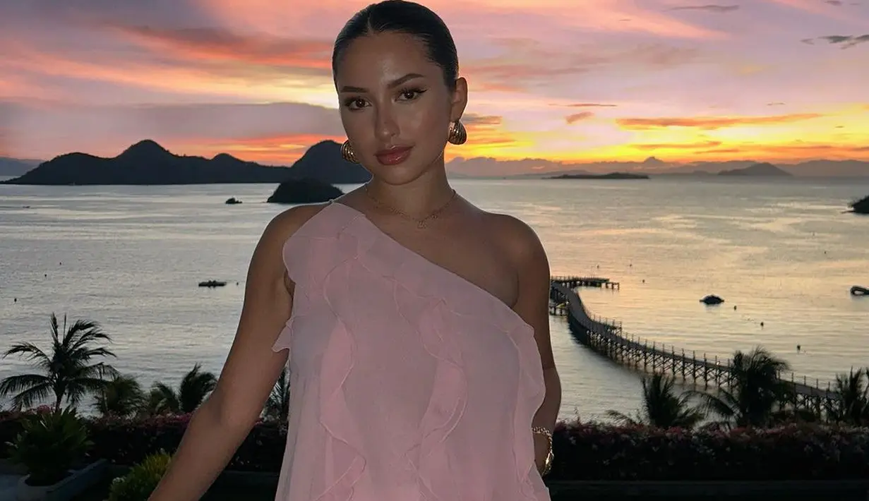 Lihat betapa memesona-nya Jennifer Coppen dibalut blouse warna pink yang selaras dengan warna matahari terbenam di belakangnya. Untuk bawahan, ia memilih shorts putih yang nyaman. [Foto: IG/Jennifercoppenreal20].