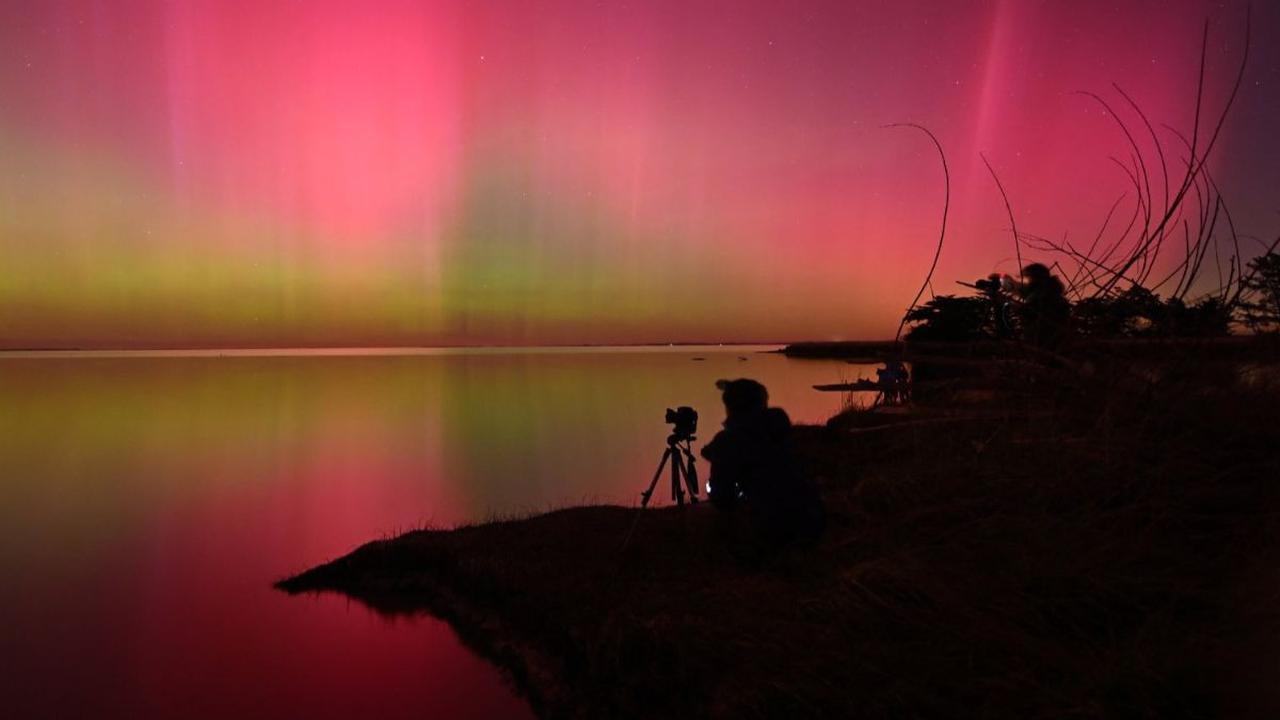Seorang fotografer mengabadikan Aurora Australis yang menghiasi langit&nbsp;di atas perairan Danau Ellesmere, Christchurch, Selandia Baru, Sabtu (11/5/2024). Terlihat begitu indah dengan warna-warni cahaya yang menari-nari, namun ternyata aurora langka in