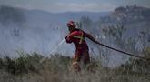 Seorang petugas pemadam kebakaran mengarahkan air ke api rumput di areal di belakang properti perumahan di Kamloops, British Columbia, Senin, 5 Juni 2023. Tidak ada bangunan yang rusak tetapi petugas pemadam kebakaran harus menghadapi kondisi angin yang sangat kencang saat memadamkan api. (Darryl Dyck/The Canadian Press via AP)