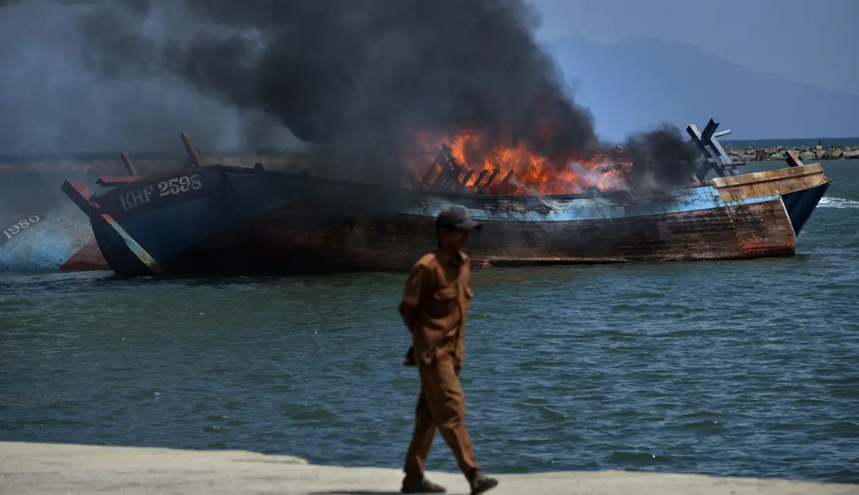 Kobaran api tampak membakar kapal asing ilegal asal Malaysia yang ditenggelamkan di perairan Pelabuhan Perikanan Samudera Kutaraja, Banda Aceh, Aceh, Kamis (18/3/2021). (AFP/Chaideer Mahyuddin)