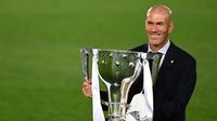 Pelatih Real Madrid, Zinedine Zidane, mengangkat trofi juara La Liga musim 2019/2020 usai timnya mengalahkan Villarreal pada laga lanjutan La liga di Estadio Alfredo Di Stefano, Jumat (17/7/2020) dini hari WIB. (AFP/Gabriel Bouys)