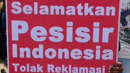 Seorang nelayan menunjukkan poster berisi penolakan terhadap proyek reklamasi Teluk Jakarta saat upacara sedekah bumi yang lebih dikenal dengan sebutan Nadran di Muara Angke, Jakarta, Minggu (13/12/2015). (Liputan6.com/Helmi Afandi)