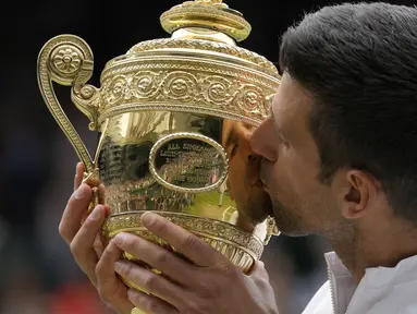 Petenis Serbia, Novak Djokovic cium Piala Wimbledon usai kalahkan petenis Italia, Matteo Berrettini di partai puncak tunggal putra. Kemenangan ini mengantarkan Djokovic menyamai rekor Nadal dan Federer sebagai petenis yang mampu mendapatkan 20 gelar Grand Slam. (Foto: AP/Kirsty Wigglesworth)