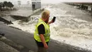 Seorang pekerja utilitas memotret ombak saat mereka menabrak tembok laut di marina kota saat band luar Badai Ida tiba di Bay Saint Louis, Miss (29/8/2021). Menurut Gubernur Louisiana John Bel Edwards, Ini adalah salah satu badai terkuat yang mendarat di sini di zaman modern. (AP Photo/Steve Helber)