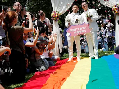 Pasangan sesama jenis berjalan di atas bendera pelangi raksasa saat melangsungkan pesta pernikahan mereka di Taipei, Taiwan, Jumat (24/5/2019). Taiwan menggelar pernikahan sesama jenis pertama di Asia. (REUTERS/Tyrone Siu)