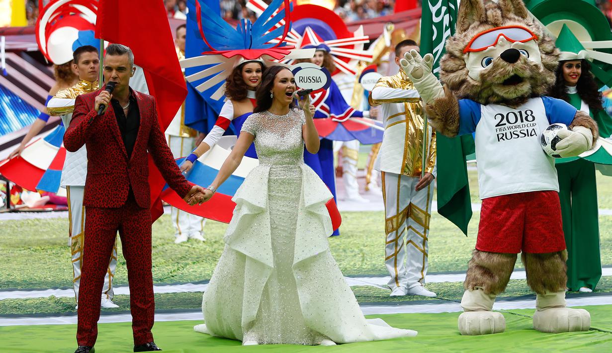 Penyanyi Inggris, Robbie Williams dan penyanyi soprano Rusia Aida Garifullina berduet pada upacara pembukaan Piala Dunia 2018 di Stadion Luzhniki, Kamis (14/6). Tak tertinggal maskot Piala Dunia 2018 Zabivaka berada di antara keduanya. (AP/Matthias Schrad