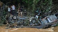 Orang-orang mencoba menyelamatkan barang-barang dari mobil yang hancur akibat banjir bandang di Petropolis, Brasil, 16 Februari 2022. Sebanyak 55 orang tewas dalam banjir bandang dan tanah longsor yang menghancurkan Kota Petropolis. (CARL DE SOUZA/AFP)