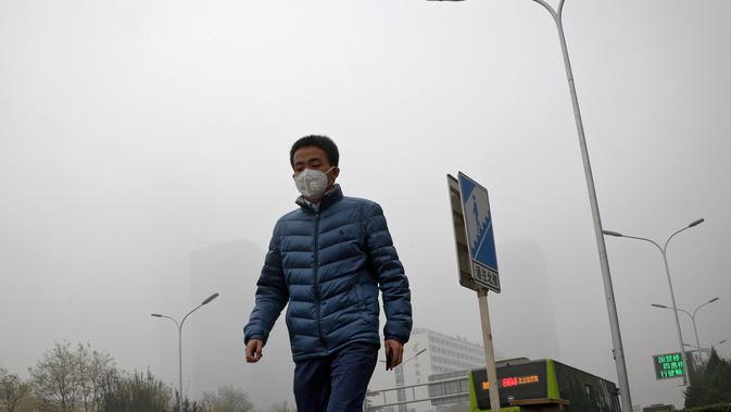 Seorang pria beraktivitas mengenakan masker di sebuah jalan yang diselimuti kabut asap tebal di Beijing, China (14/11). Pihak berwenang mengeluarkan peringatan kuning untuk polusi udara buruk pada hari Rabu. (AP Photo/Andy Wong)