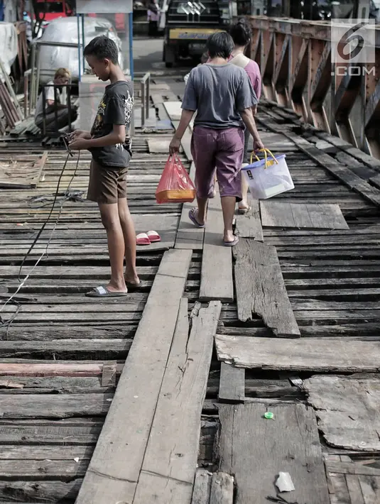 Warga melintasi jembatan dari kayu yang menjadi penghubung antara Jalan Karet Pasar Baru VII, Karet Tengsin dan Jalan Pam Baru, Bendungan Hilir, Tanah Abang, Rabu (30/1). (Liputan6.com/Faizal Fanani)