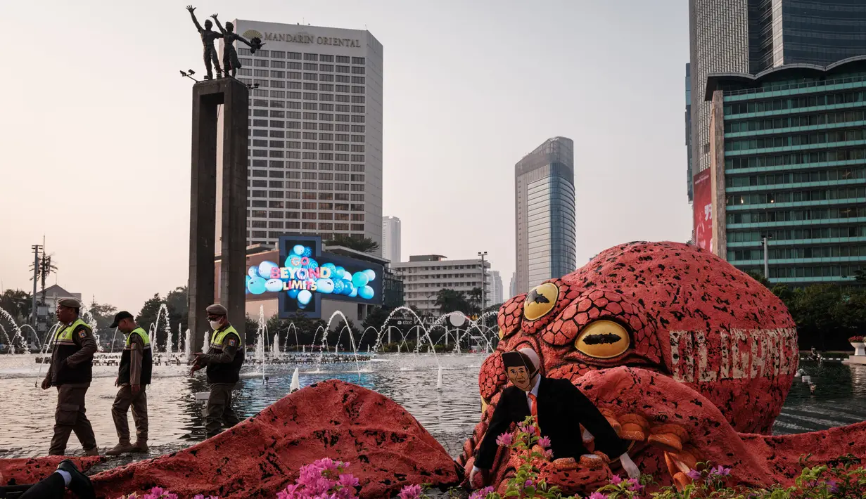 <p>Polisi berjalan melewati sosok berbentuk gurita yang memegang manekin yang menyerupai seorang bakal calon presiden pada pemilu 2024 mendatang di kawasan Bundaran Hotel Indonesia, Jakarta, Jumat (6/10/2023). (Yasuyoshi CHIBA/AFP)</p>