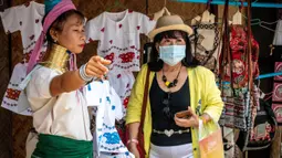 Perempuan Suku Kayan berbicara dengan turis yang mengenakan masker di sebuah toko suvenir di Taman Chang Siam, Pattaya, Thailand, Rabu (12/2/2020). Chang Siam Park adalah salah satu primadona bagi wisatawan China di Pattaya  yang kini berangsur sepi karena virus corona. (Mladen ANTONOV / AFP)