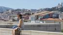 Seorang wanita duduk dengan latar belakang suasana kota di Marseille, Prancis, Minggu (3/7/2016). Marseille merupakan daerah pesisir di selatan Prancis dengan pesona keindahan alam. (Bola.com/Vitalis Yogi Trisna)