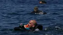 Seorang pengungsi Suriah membawa bayi menggunakan pelampung dan berenang menuju pantai setelah perahu yang ditumpangi bocor sekitar 100 m sebelum mencapai pulau Lesbon, Yunani, Minggu (13/09/2015). (REUTERS/Alkis Konstantinidis) 