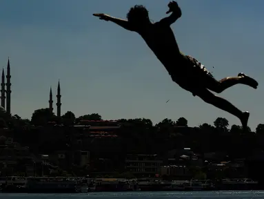 Berlatar belakang Masjid Suleymaniye yang bersejarah, seorang pemuda melompat ke Tanduk Emas (golden horn) mengarah ke Selat Bosphorus yang memisahkan Eropa dan Asia, di Istanbul, Turki pada 3 Juli 2020. (AP Photo/Emrah Gurel)