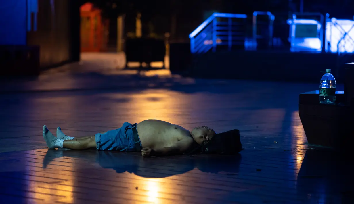 Seorang pria tidur di lantai di sepanjang Nanjing East Road, Shanghai (8/8). Nanjing East Road yang biasanya ramai oleh pembeli dan turis berubah menjadi pesta tidur terbuka pada malam hari. (AFP Photo/Johannes Eisele)