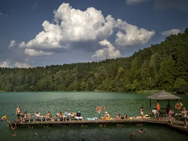 Orang-orang menikmati cuaca hangat di tepi danau dekat Vilnius, Lituania, Kamis, 17 Agustus 2023.(AP Photo/Mindaugas Kulbis)