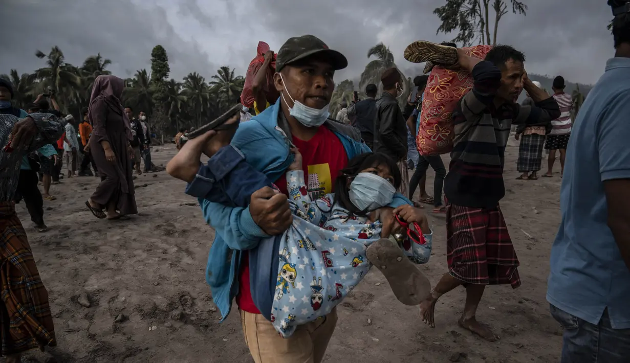 Seorang warga membawa seorang anak ketika orang-orang menyelamatkan barang-barang mereka di daerah yang tertutup abu vulkanik setelah letusan gunung berapi Semeru di desa Sumber Wuluh di Lumajang, Jawa Timur, Minggu (5/12/2021). (AFP /Juni Kriswanto)