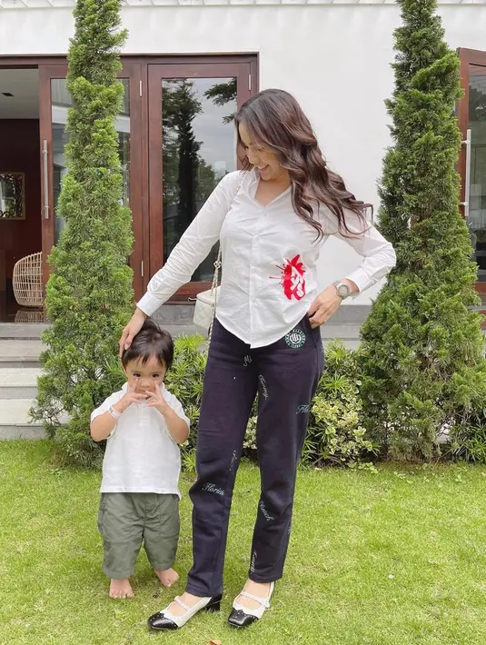 Di sini, Momo mengenakan outfit serasi dengan sang buah hati. Momo mengenakan kemeja berwarna putih dengan motif minimalis, dipadunya dengan celana panjang hitam yang juga bermotif minim. Foto: Instagram.