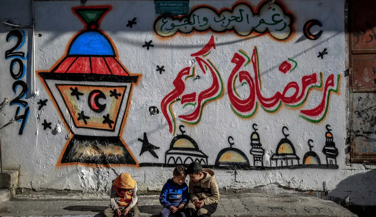 Anak-anak Palestina duduk di depan tembok dengan gambar bertema Ramadan di Kota Gaza pada 8 Maret 2024. (Foto: AFP)