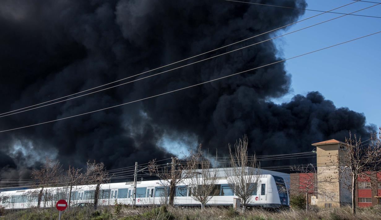 Kereta melintas di dekat perusahaan kimia Indukern yang sedang terjadi kebakaran di kawasan industri Fuente del Jarro, Paterna, Valencia, Spanyol, Rabu (8/2). (AFP PHOTO / Biel Alino)