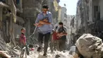 Para pria menggendong bayi saat berjalan melewati puing-puing bangunan yang hancur usai serangan udara di daerah yang dikuasai pemberontak di Salihin, Aleppo, Suriah, 11 September 2016. (Photo by Ameer al-HALBI/AFP)