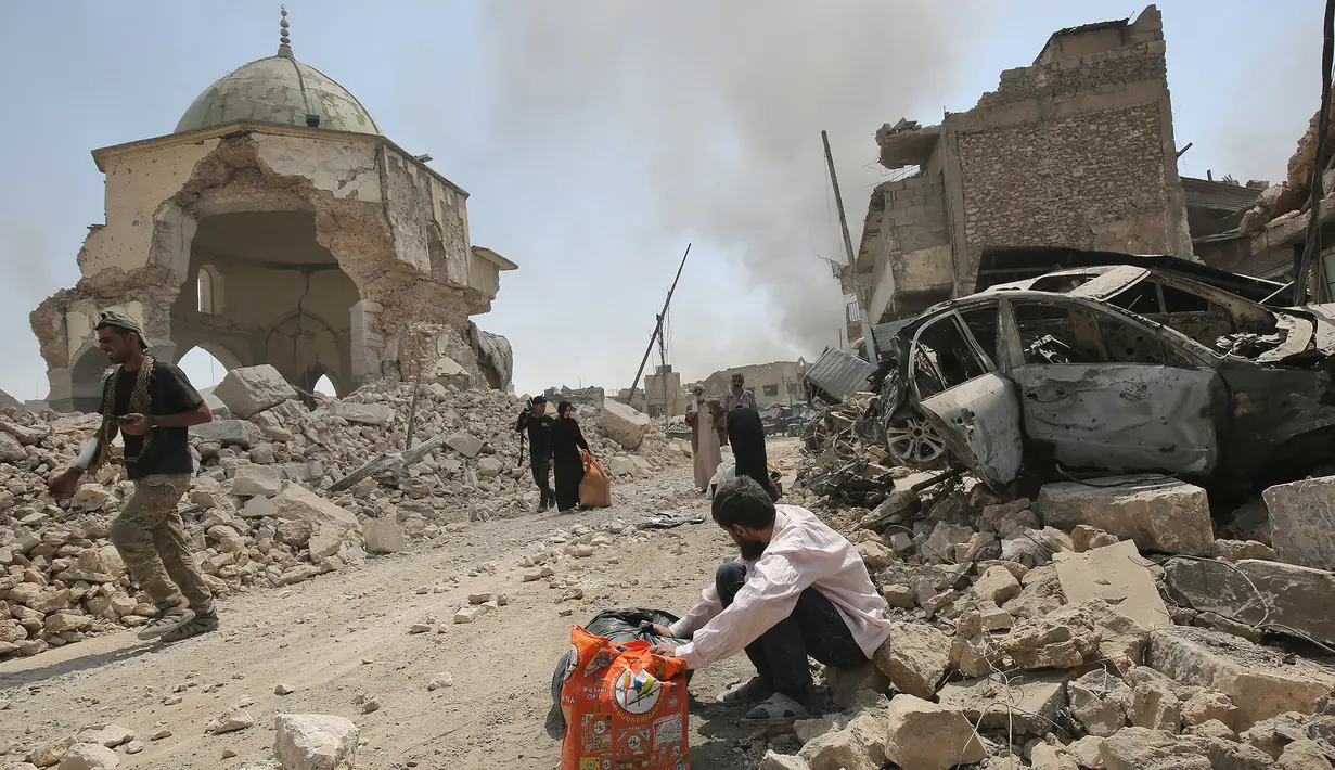 Warga sipil Irak melewati Masjid Agung al-Nuri yang hancur saat mengungsi dari Kota Tua di Mosul, 30 Juni 2017. Masjid yang dibangun pada abad ke-12 ini diledakkan ISIS pada 21 Juni 2017 sebagai upaya menghambat laju pasukan Irak. (AHMAD AL-RUBAYE/AFP)