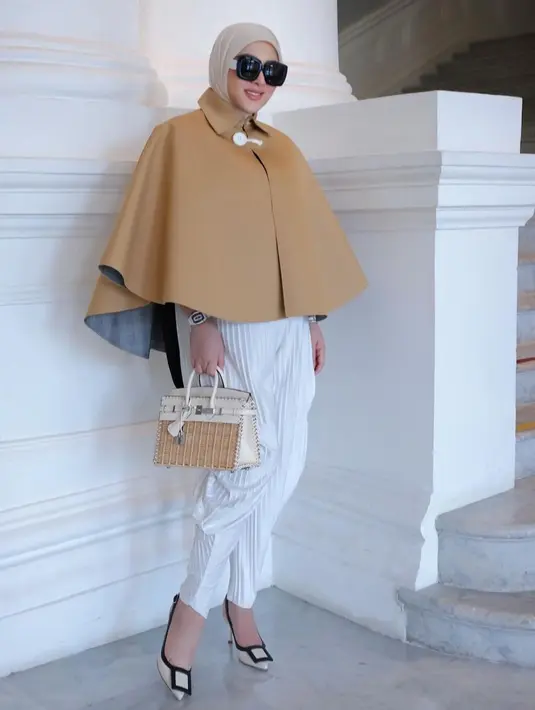 Padu padan chic Syahrini di foto ini. Ia mengenakan top bersiluet cape berwarna cokelat dipadu pleated pants putih, dan hijab cokelat muda polos, tas bernuansa senada, dan high heels nude. [Foto: Instagram/princessyahrini]